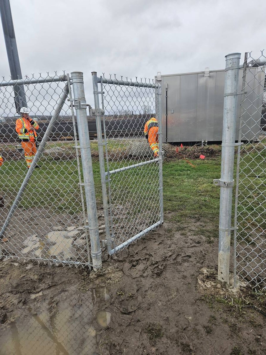 Crew installing a chain link access gate on a muddy rail corridor site